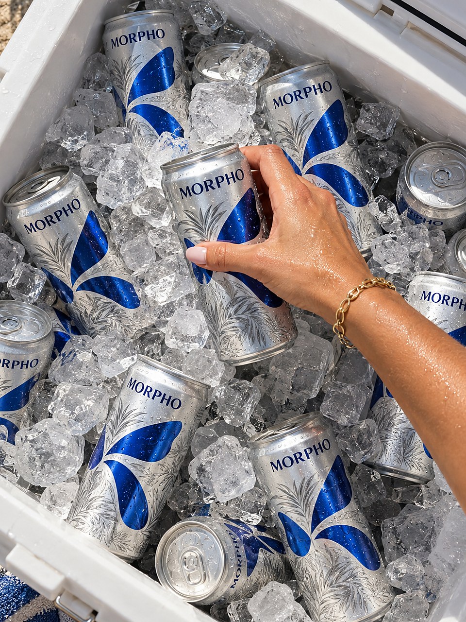 A hand reaching for a MORPHO can in a cooler filled with cans and ice